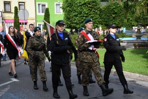 Ubrane w mundury dwie kobiety i mężczyzna, niosący flagę Polski