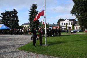 Mężczyzna w mundurze, wciągający flagę Polski na maszt