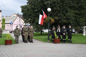 Stojący w kolumnach uczniowie w mundurach wojskowych i strażackich