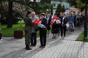 Mężczyzna i kobieta, przekazujący kwiaty kobiecie w mundurze, w tle ludzie