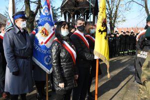 Troje ludzi, stojących ze sztandarem, w tle policjant