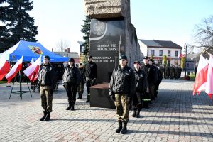 Grupa ludzi w mundurach, stojąca przed pomnikiem