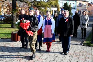 Kobieta w mundurze z kwiatami, w tle para w kujawskich strojach