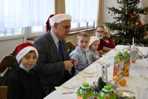 Dzieci i starosta J. Kołtuniak siedzą przy stole ze słodkościami