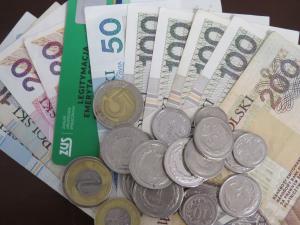 Rozłożone banknoty w polskiej walucie, w tle zielona legitymacja emeryta i rencisty