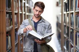 Mężczyzna z książką, stojący między regałami w bibliotece