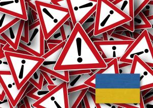Znaki ostrzegawcze z wykrzyknikami, w rogu flaga Ukrainy