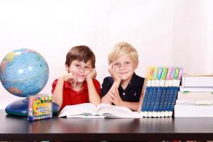 Dwóch chłopców, siedzących przy biurku, otwarta książka i globus